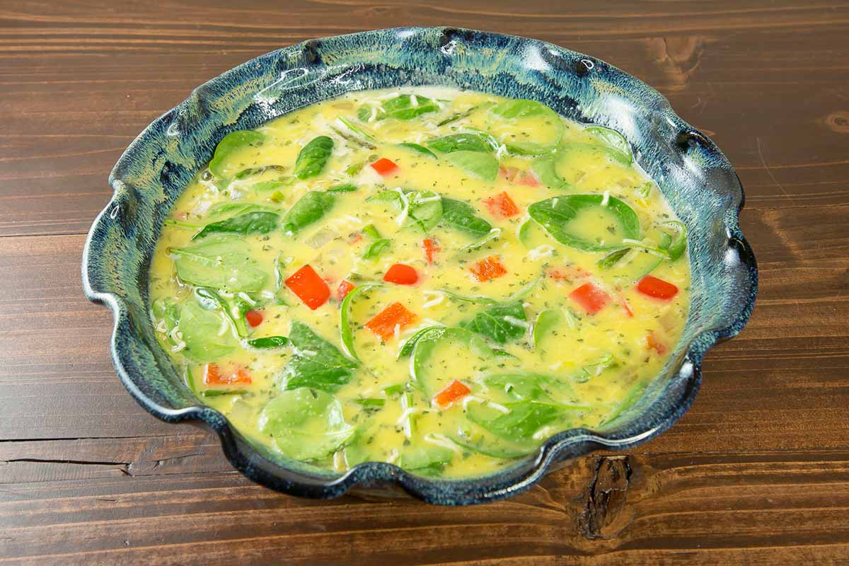 Horizontal image of a raw vegetable and egg mixture in a pie plate.