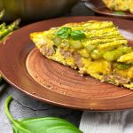 Horizontal close-up image of a wedge of vegetable and meat frittata on a brown plate.