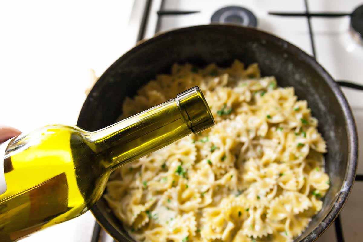 Horizontal image of pouring alcohol from a bottle into a large pot with farfalle pasta.