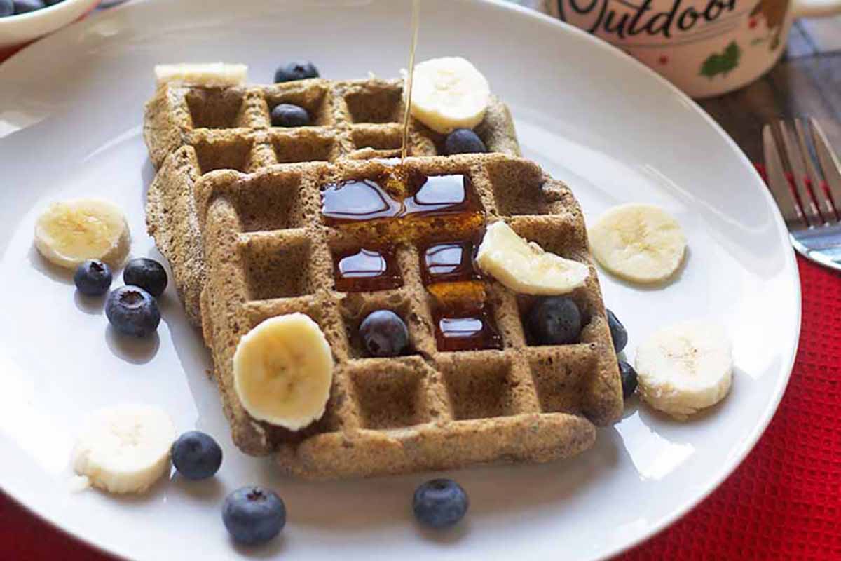 Horizontal image of two buckwheat waffles on a plate with a drizzle of maple syrup.