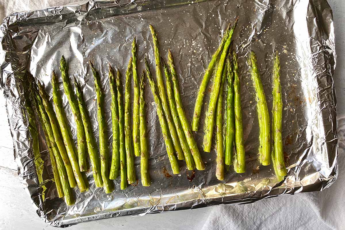 Horizontal image of roasted asparagus on a baking sheet lined with aluminum foil.