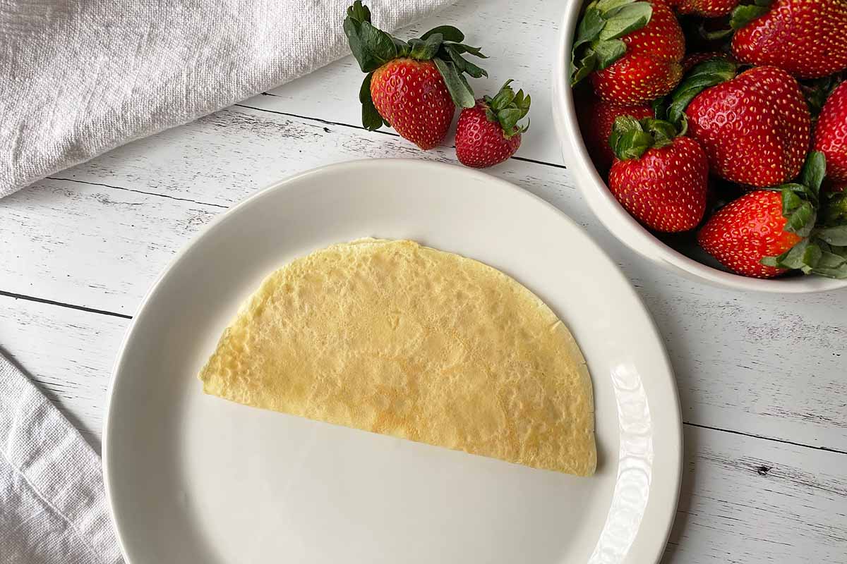 Horizontal image of a thin pancake folded in half on a white plate.