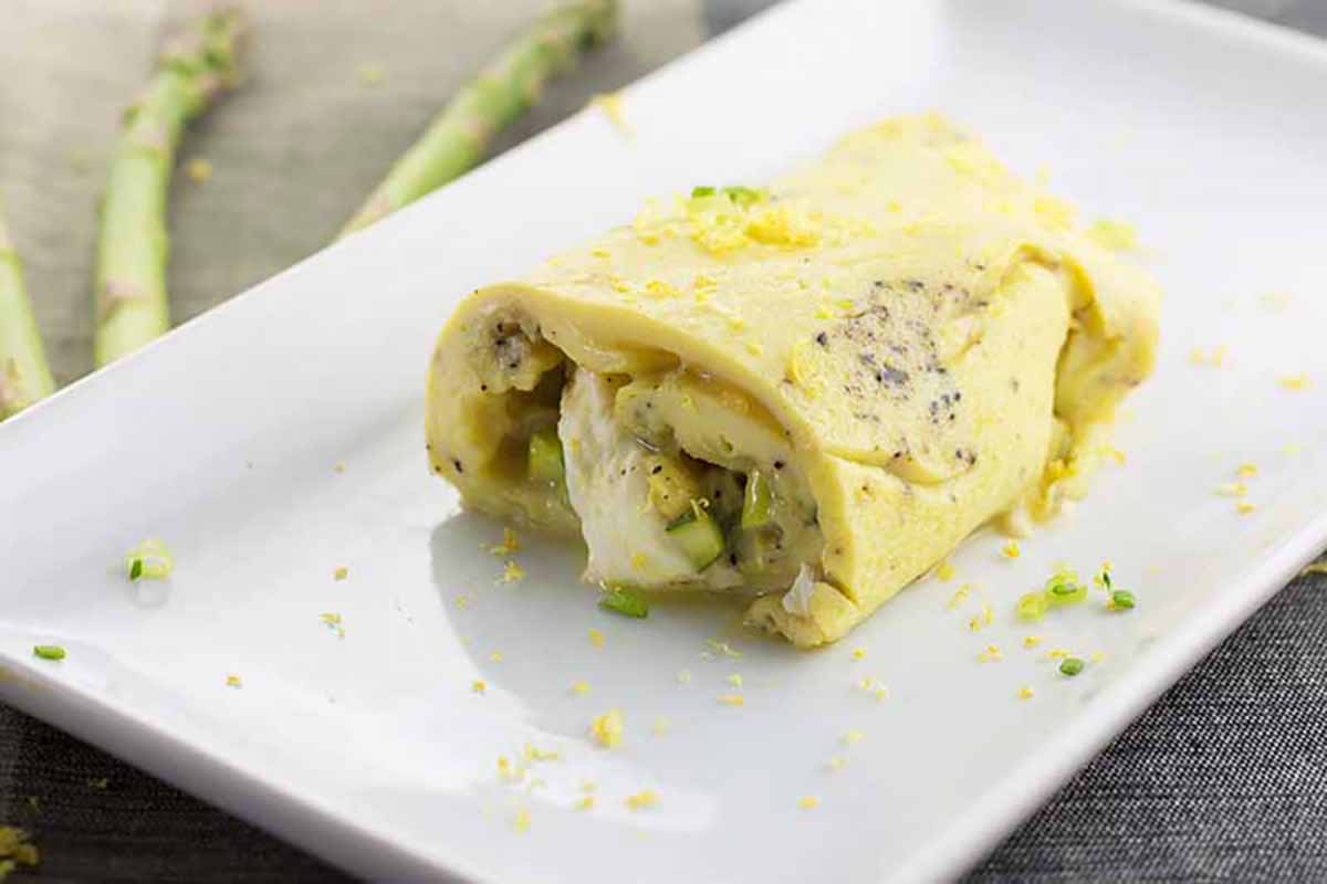 Horizontal image of an omelet filled with asparagus and mozzarella cheese on a white rectangular plate.