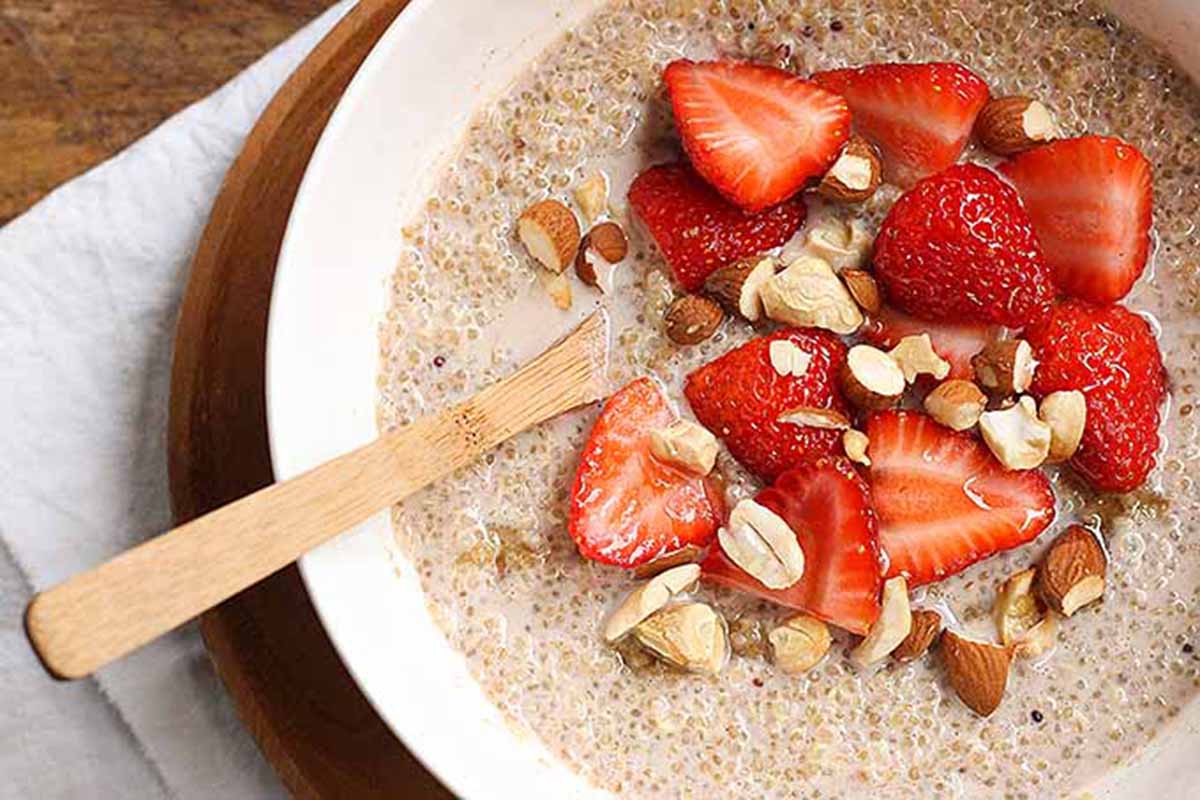 Horizontal image of a hot quinoa porridge garnished with nuts and sliced strawberries.