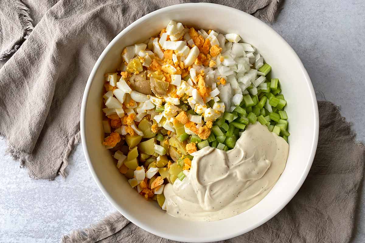 Horizontal image of piles of ingredients in a large bowl, with a creamy dressing.