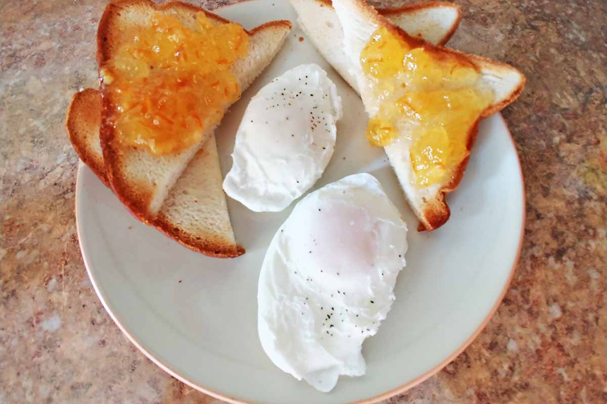 Horizontal image of poached eggs next to toast spread with marmalade.