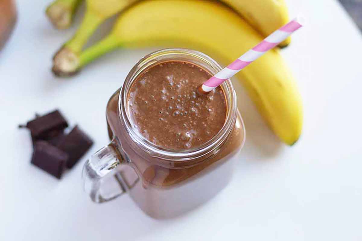 Horizontal image of a mason jar with a handle filled with a chocolate smoothie with a straw inserted into it.