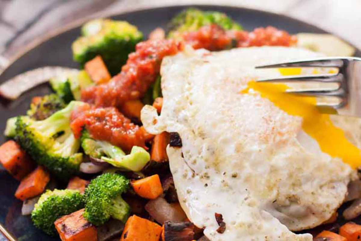 Horizontal image of breaking into an egg over a bed of broccoli and sweet potatoes with salsa.