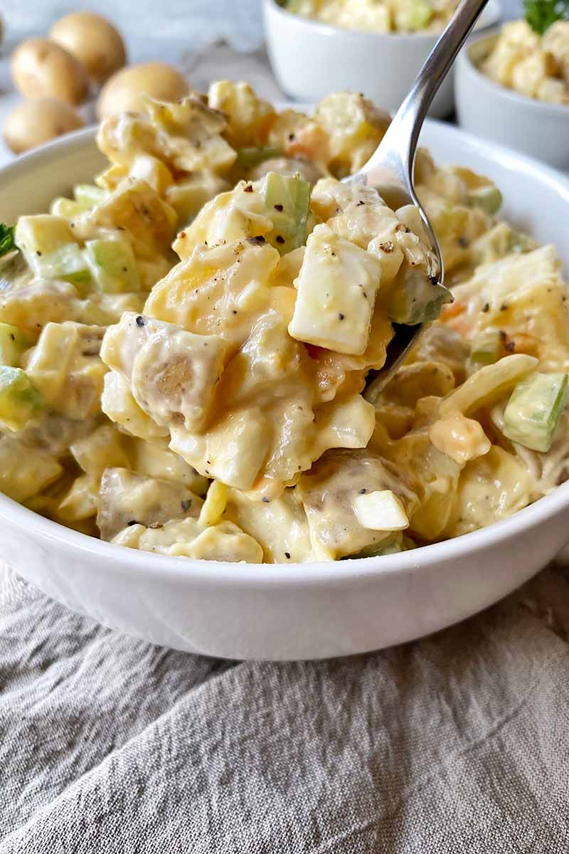 Vertical close-up image of a spoonful of potato salad over a large serving bowl.