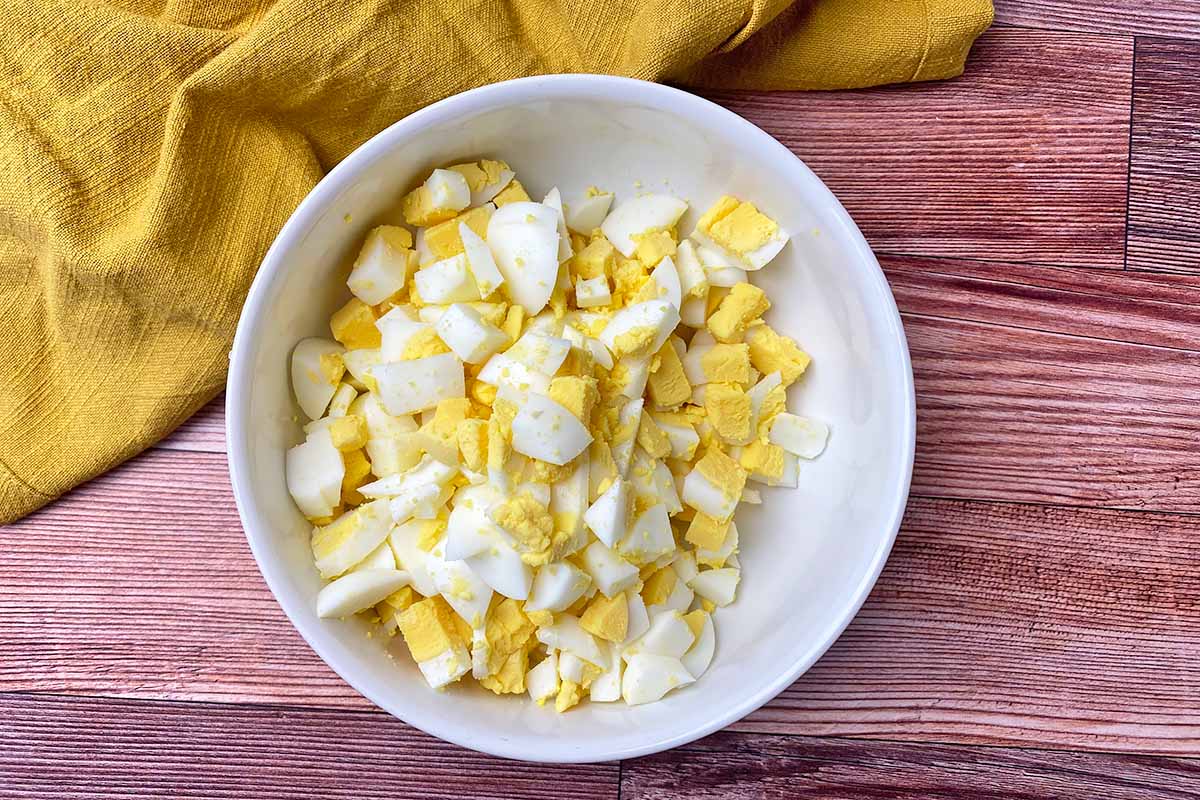 Horizontal image of roughly chopped hard-boiled yolks and whites in a white bowl next to a yellow towel.