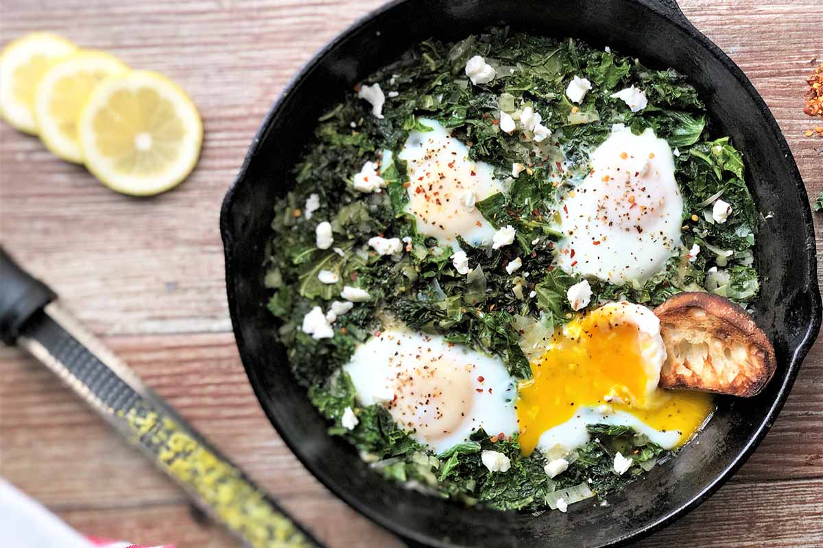 Horizontal image of a bed of kale in a skillet topped with gently cooked eggs.