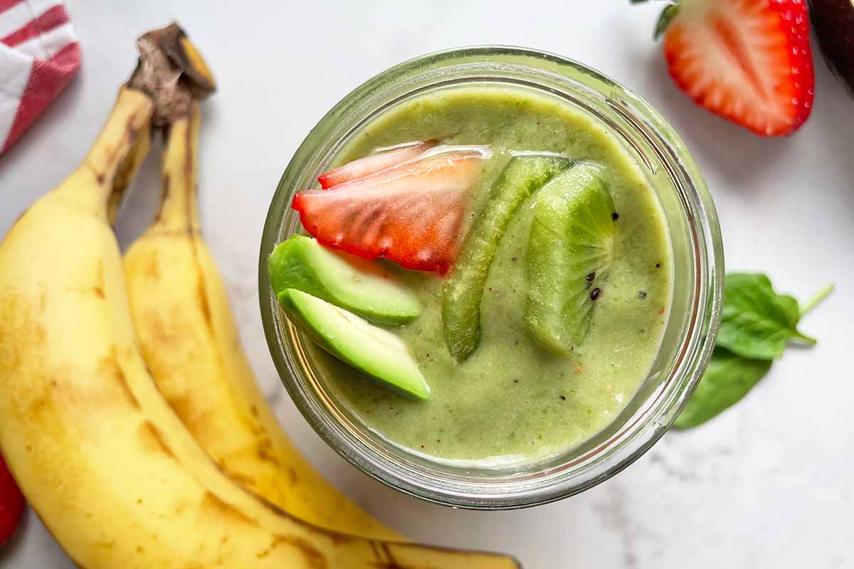 Horizontal image of a green creamy drink topped with avocado, kiwi, and strawberries.