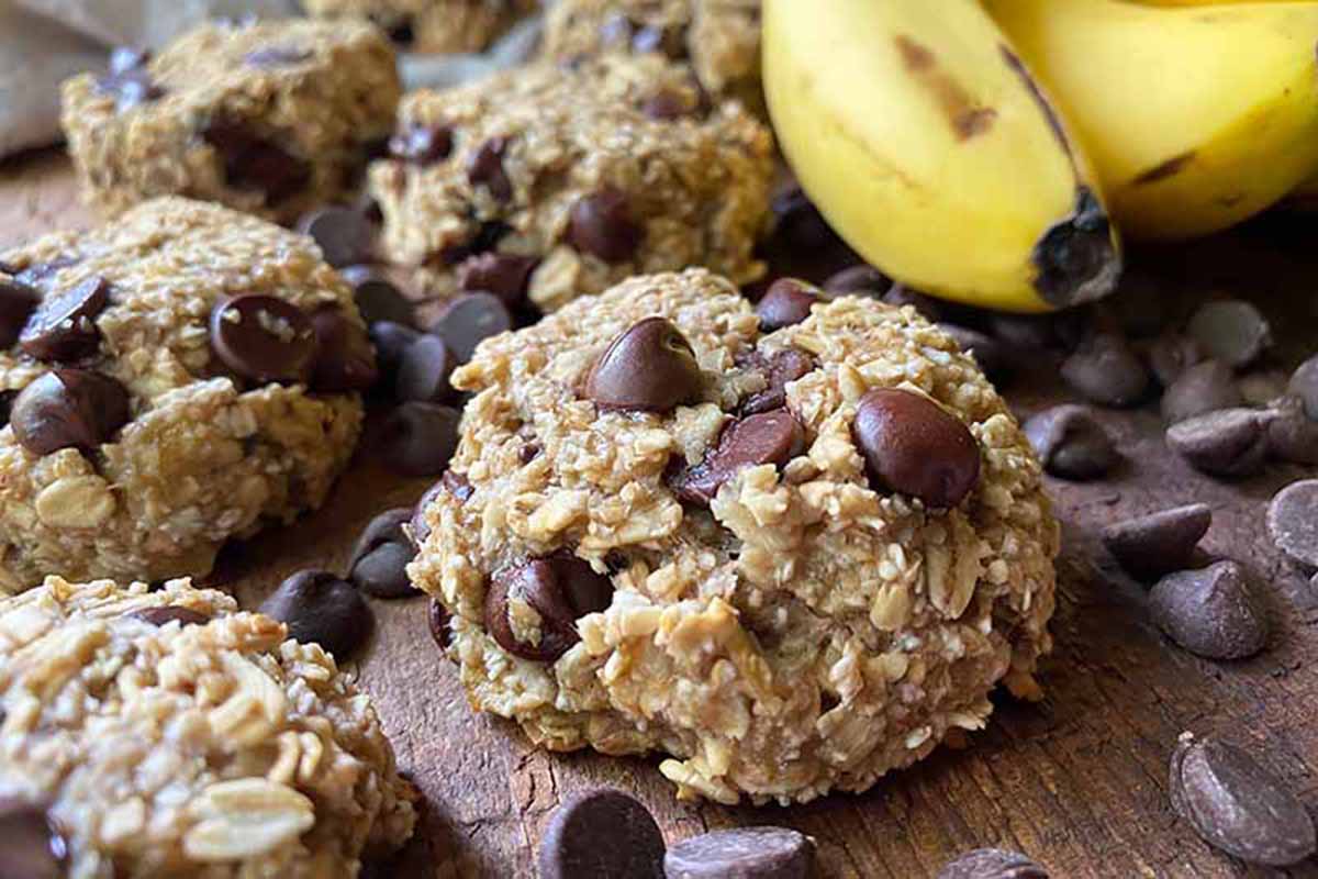 Horizontal image of a scattering of oatmeal banana chocolate chip cookies on a wooden surface.