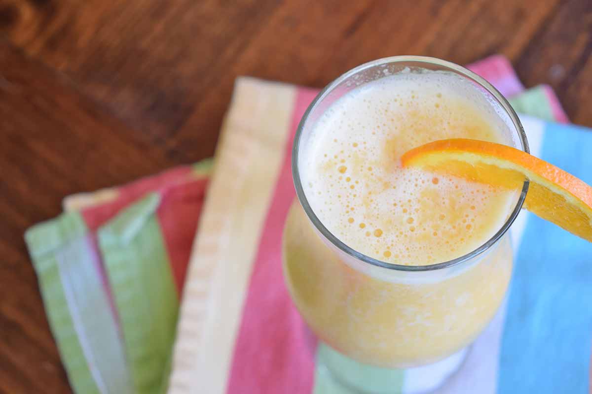 Horizontal image of a frothy orange drink in a glass with an orange slice garnish.