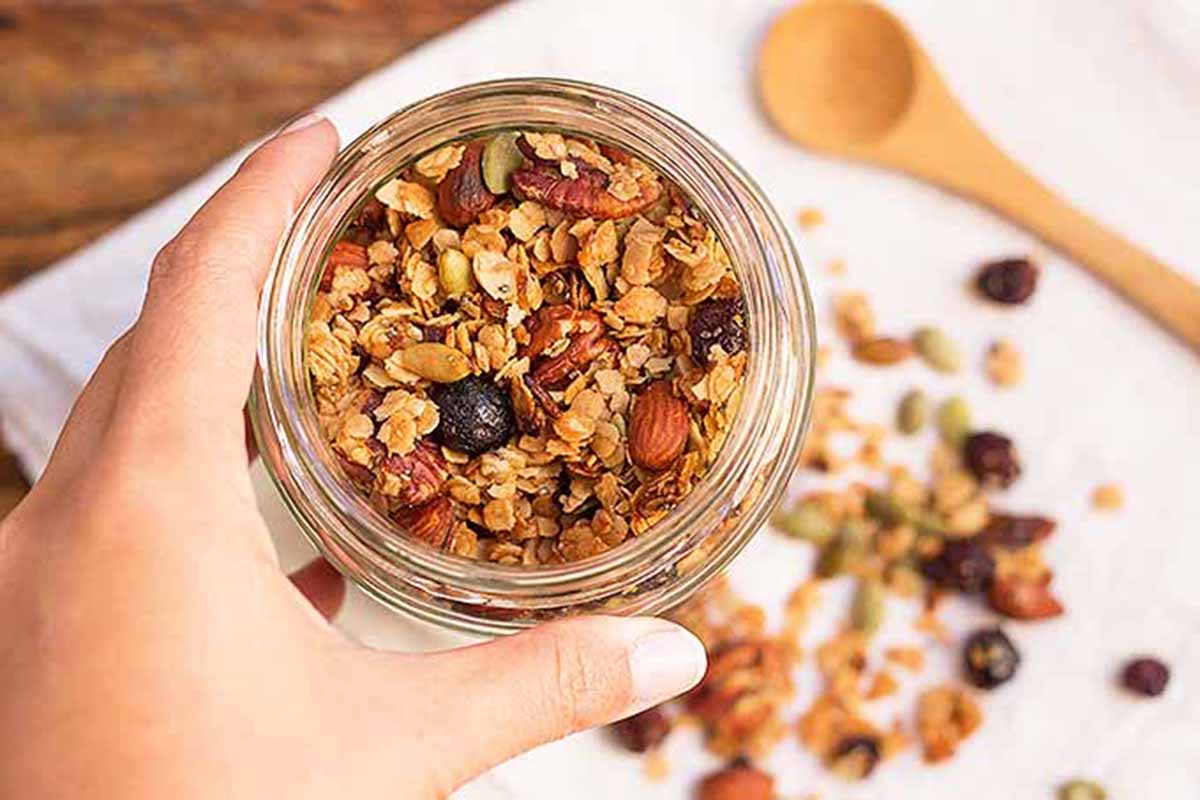 Horizontal image of granola in a jar with a hand holding the jar.
