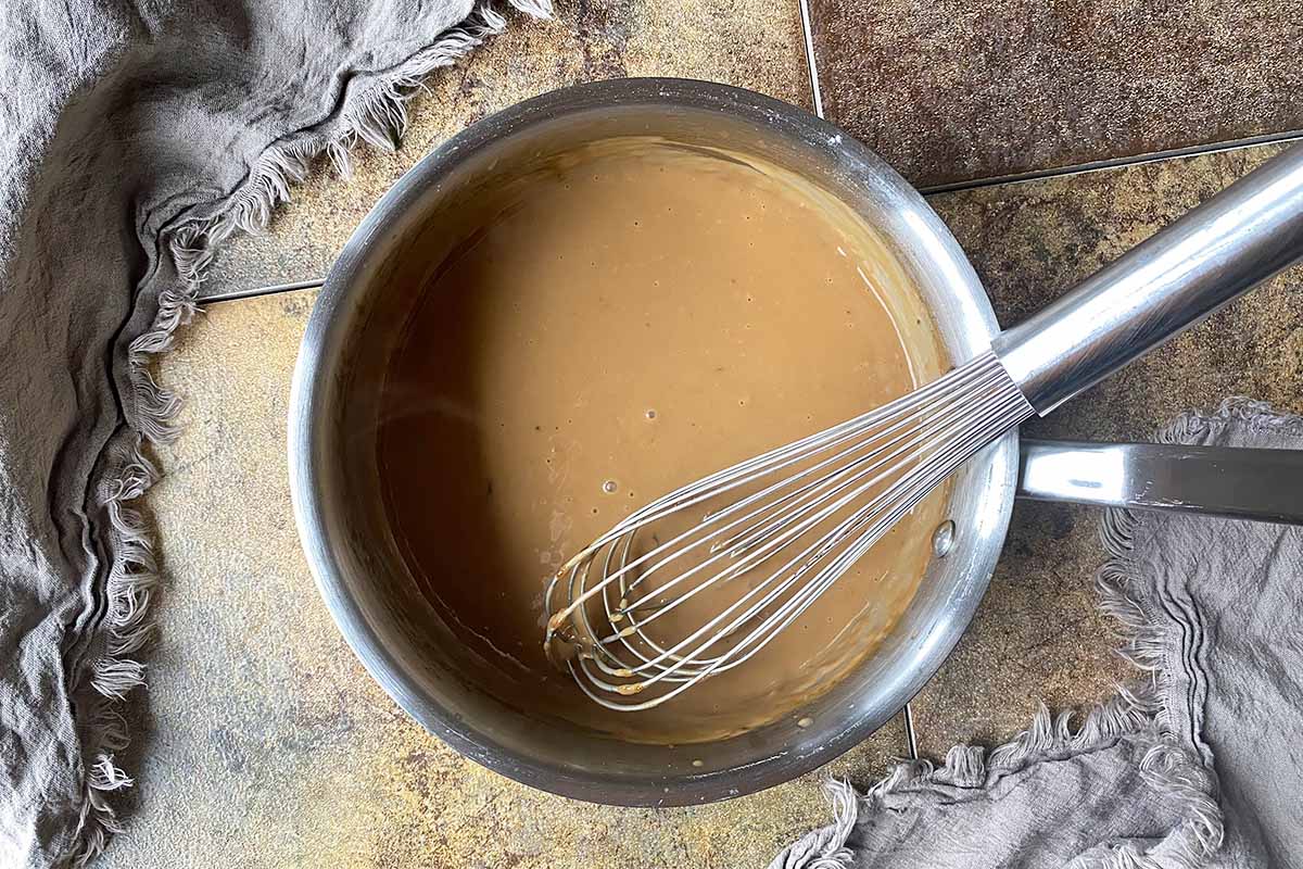 Horizontal image of a whisk over a pot with gravy.