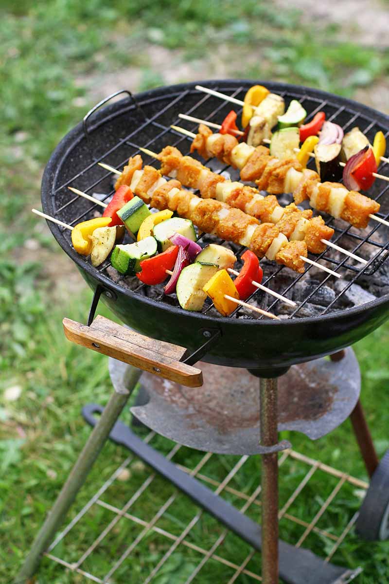 Vertical image of preparing assorted meat and vegetable kebabs outside.