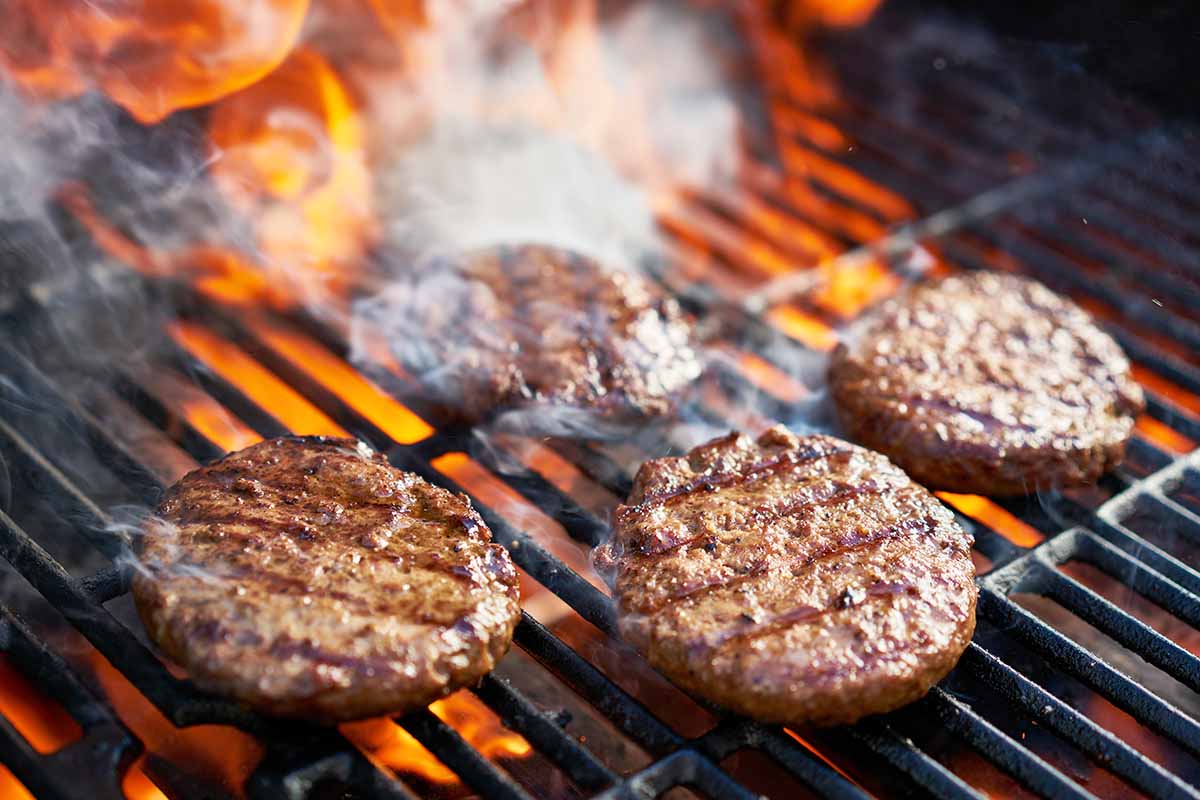 Horizontal image of preparing burgers over hot flames.