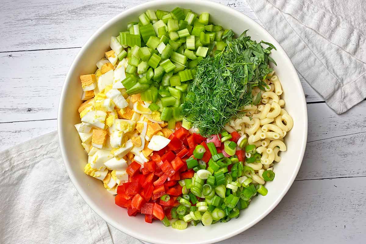 Horizontal image of assorted prepped vegetables and ingredients in a large white bowl.