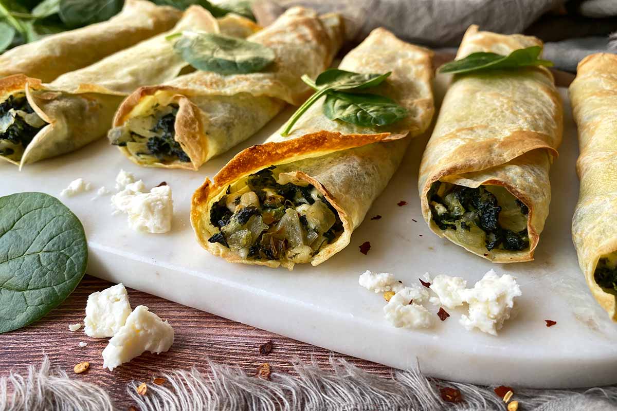 Horizontal image of rolled French thin pancakes with a greens and onion stuffing on a serving platter.