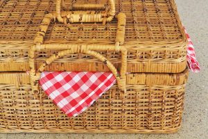 Horizontal image of a packed picnic basket with a checkered red and white towel on a countertop.