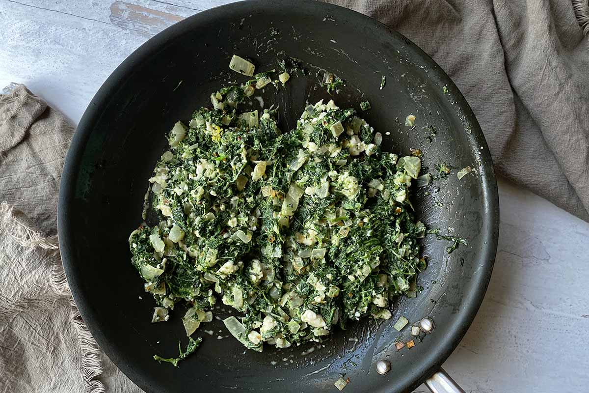 Horizontal image of a creamy greens and onions mixture in a skillet.