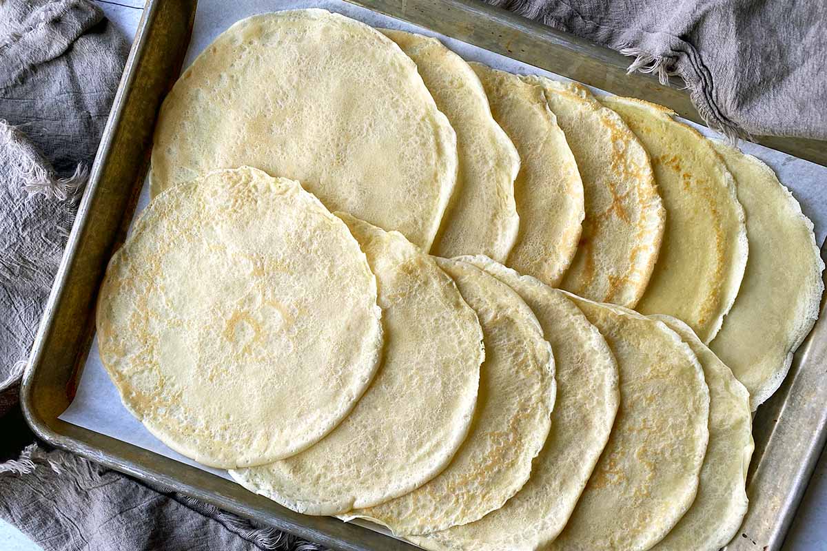 Horizontal image of shingled thin French pancakes on a baking sheet lined with parchment paper.