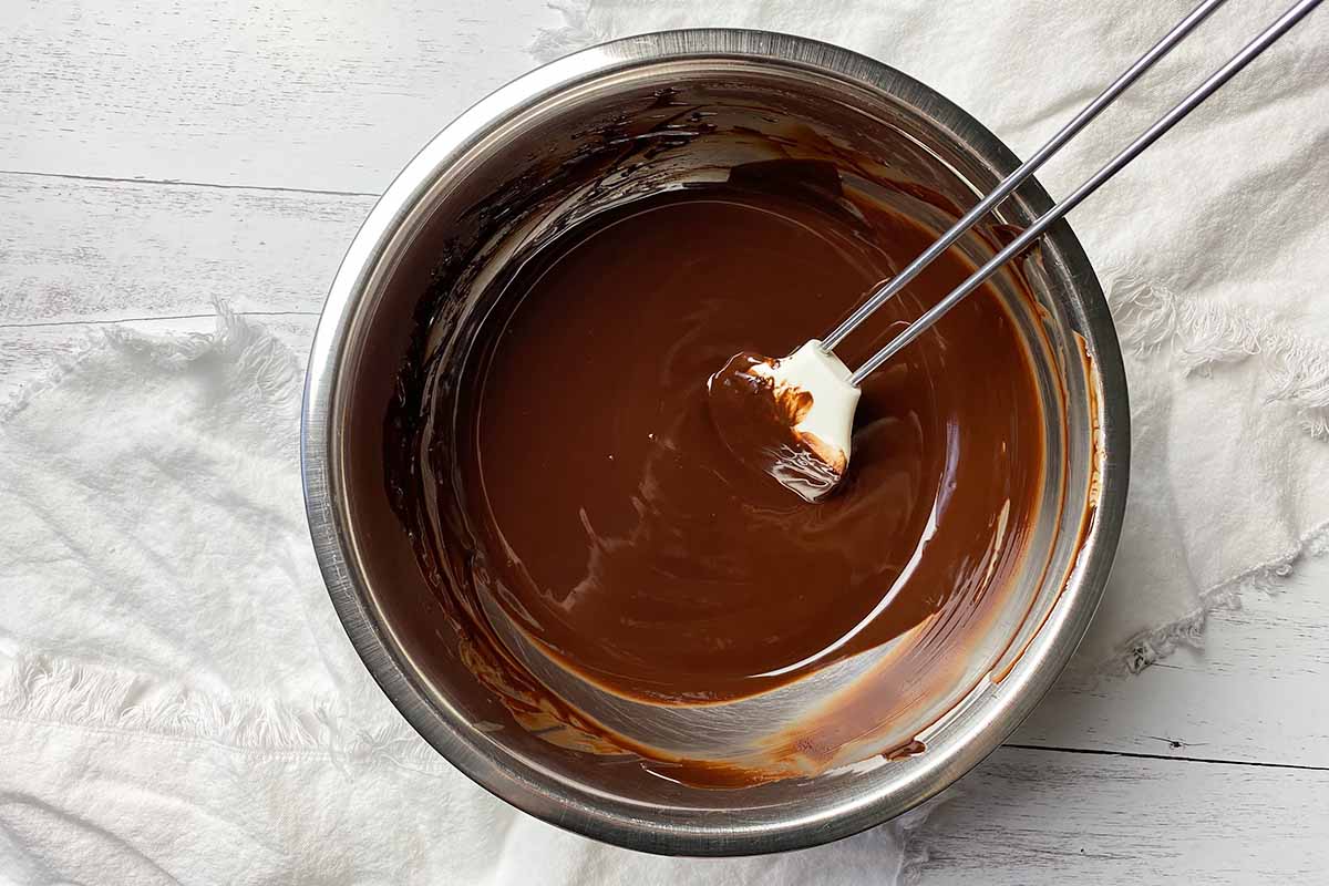 Horizontal image of melted chocolate in a metal bowl stirred with a spatula.