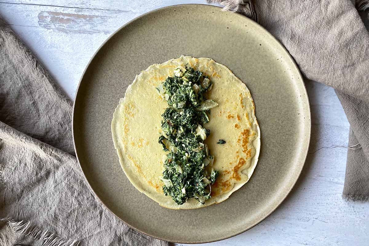 Horizontal image of assembling a thin pancake with a creamy greens mixture in the middle.