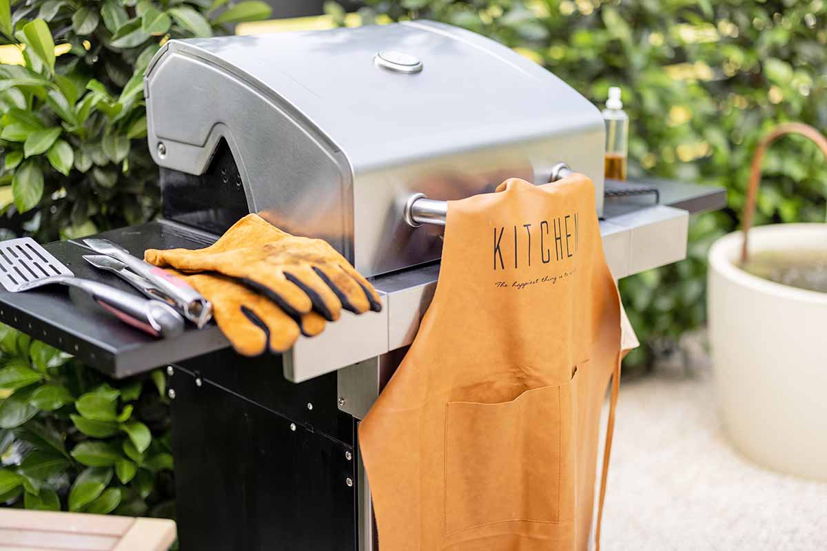 Horizontal image of gloves, an apron, and assorted BBQ equipment outdoors.