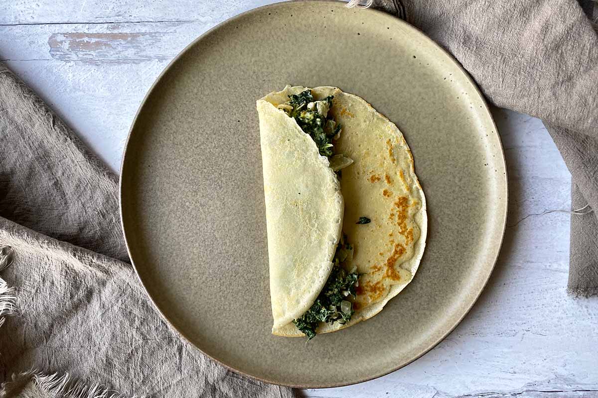 Horizontal image of assembling a thin pancake with a greens and feta mixture inside.